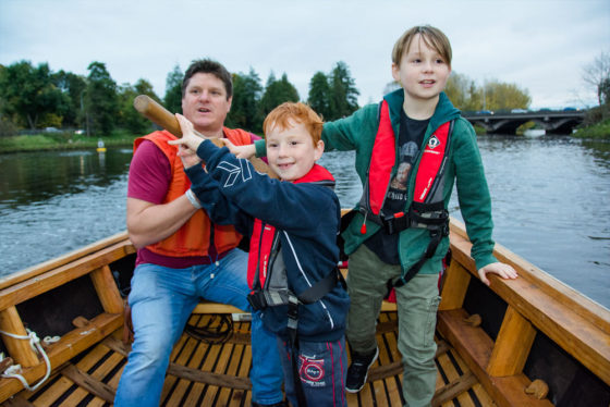 Lagan Currachs team member Tim shows young boys how to steer a currach - photo 9245. Featured image.