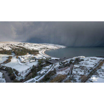 Aerial photograph of Cushendun village and Cushendun Bay, Northern Ireland, in winter under snow and storm clouds by Bout Yeh photographers Belfast. Photo 230121