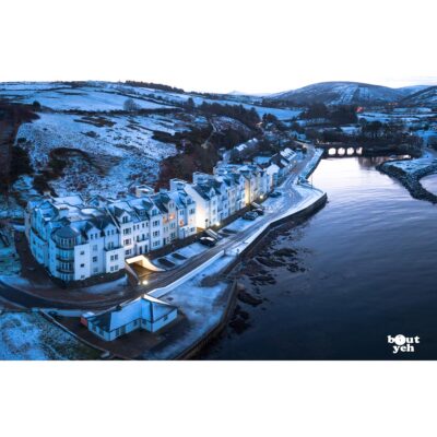Aerial photograph of Bay Apartments Cushendun, Northern Ireland, in winter under snow by Bout Yeh photographers Belfast. Photo 231121