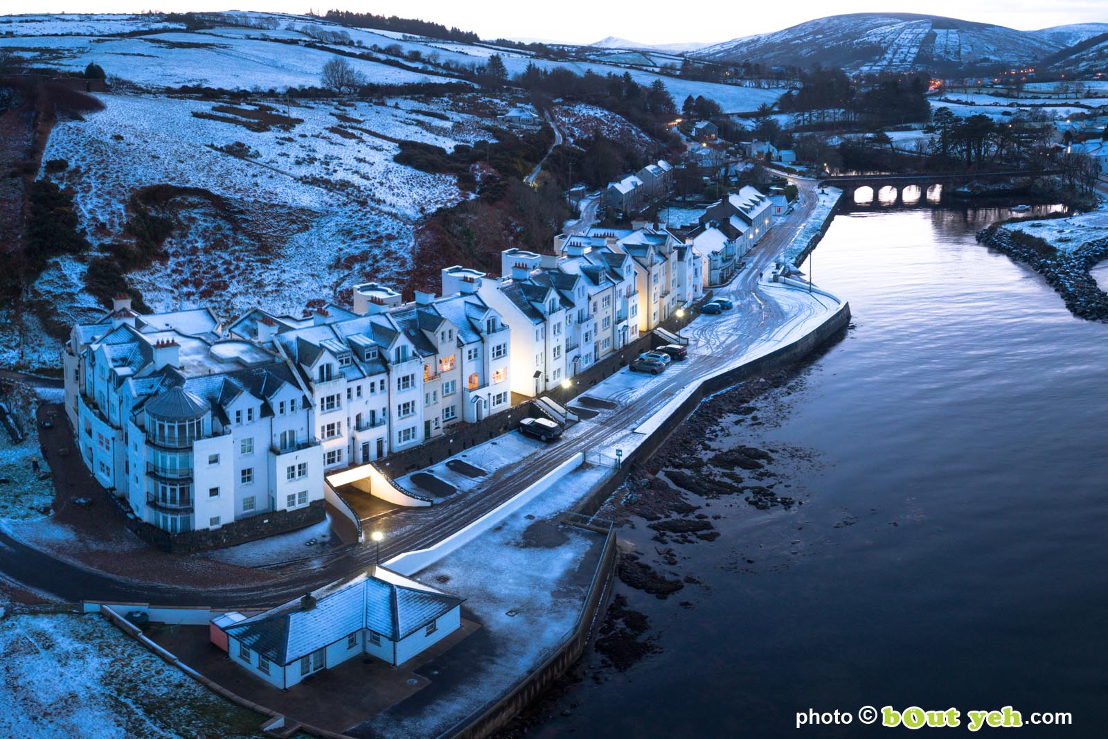 Aerial photograph of Bay Apartments Cushendun, Northern Ireland, in winter under snow at dusk by Bout Yeh photographers Belfast. Photo 231121